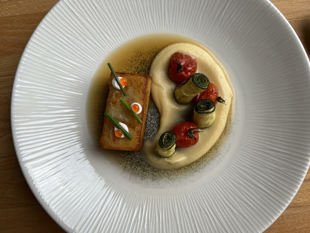 weißer Teller mit Brühe, Gratin und Püree mit Tomaten und aufgerollter Zucchini