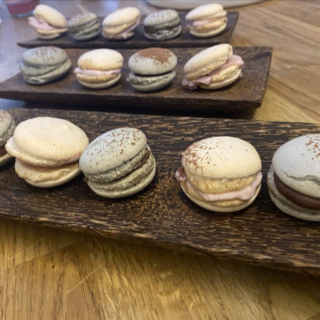 2 Gelbe und 2 grüne Macarons auf einem länglichen Holzteller, im Hintergrund nochmal zweier solcher Teller