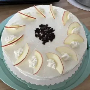 weiße Torte, dekoriert mit Apfelstücken, Sahnehäubchen und Schokoraspel