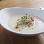Weiße Suppe mit Sprossen und Haselnüssen dekoriert
