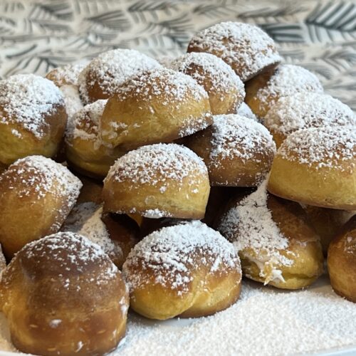 Windbeutel auf einem Teller gehäuft, mit Puderzucker bestreut